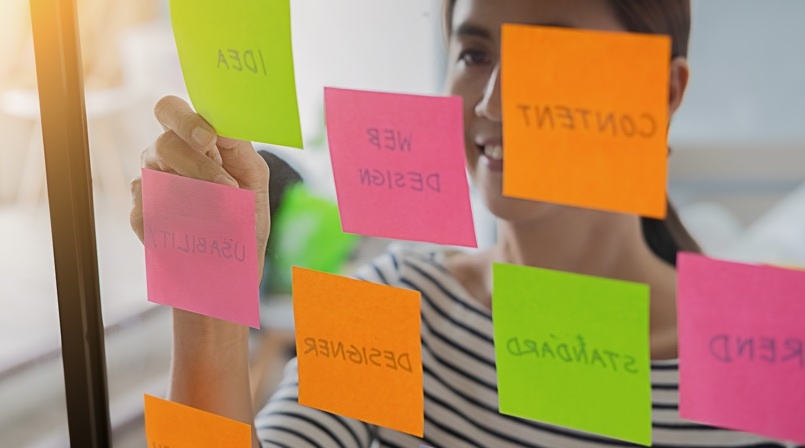 Woman writing on post it - UX Research - All you need to know about UX Design